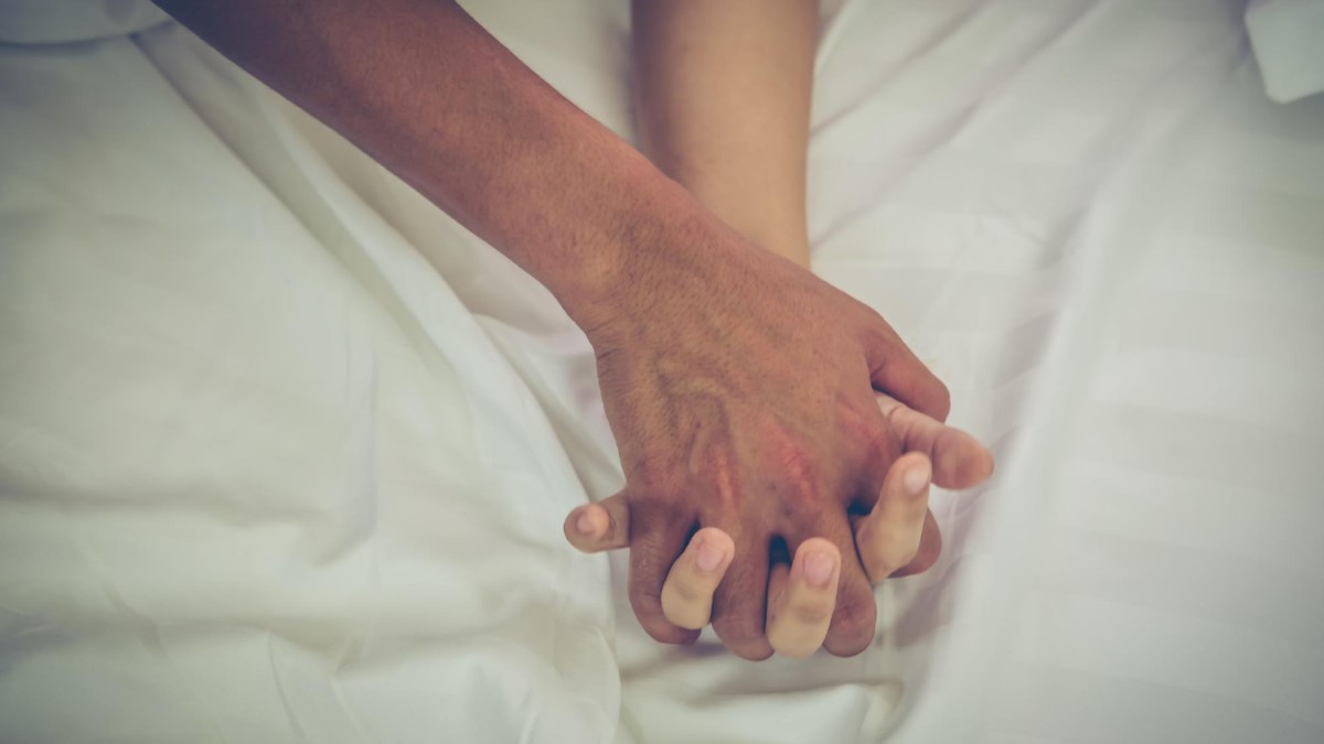 Deux mains enlacées sur un drap, ambiance romantique